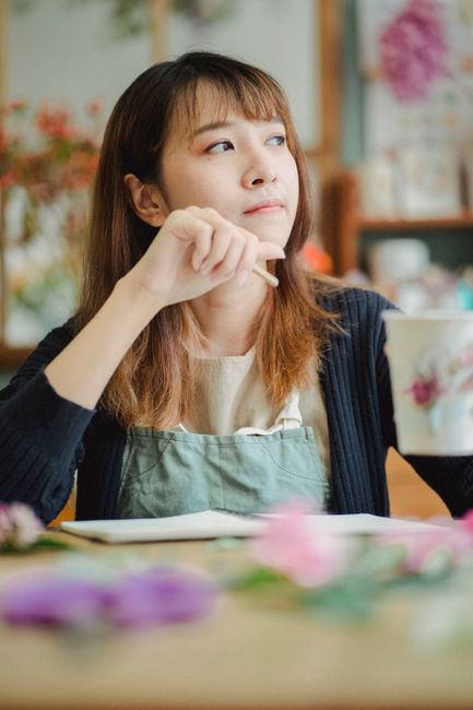 A florist from southnorwoodflorist.co.uk is arranging a bouquet of fresh flowers on a wooden table. The bouquet features a vibrant mix of roses, lilies, and daisies in shades of pink, purple, and whit